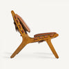 Vista lateral del Sillón de piel y madera de fresno Alford, una silla de madera de mediados de siglo con cojines y correas de cuero natural. La silla presenta un asiento reclinado y patas en ángulo sobre un fondo blanco, lo que demuestra su comodidad y estilo atemporal.