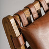 Primer plano del Sillón de piel y madera de fresno Alford, que destaca sus correas de piel marrón y cojines de piel natural. Su exquisita textura y artesanía resaltan sobre un fondo neutro, con un toque de diseño art déco.