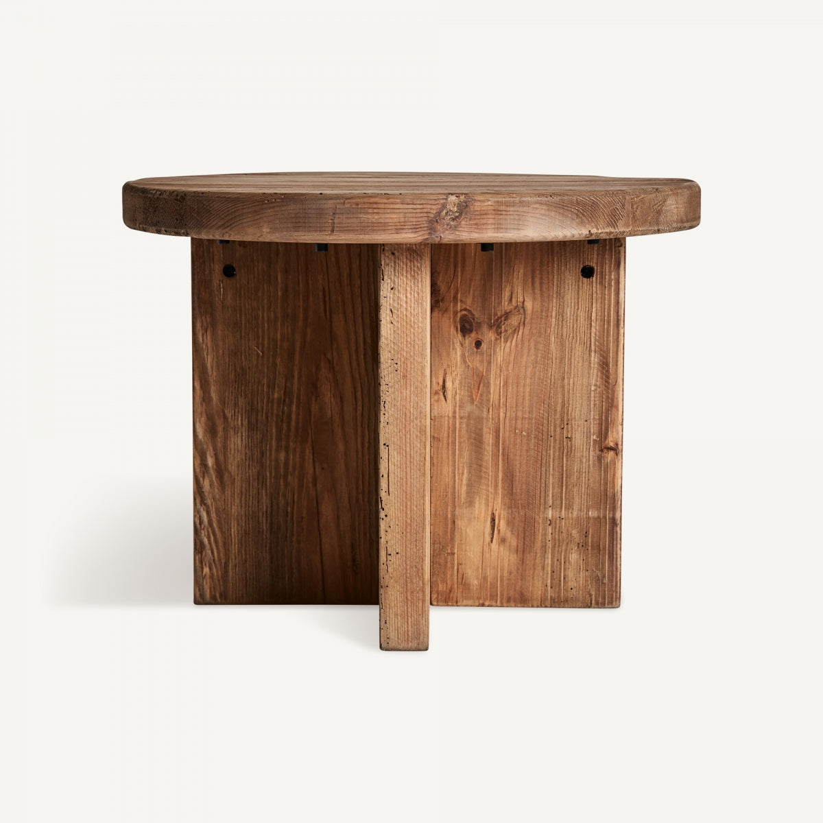 La mesa auxiliar en madera de pino reciclado Crissey presenta una tapa redonda y una base en forma de cruz con un acabado natural y veta de madera visible, incorporando el diseño contemporáneo a través de su artesanía sustentable.