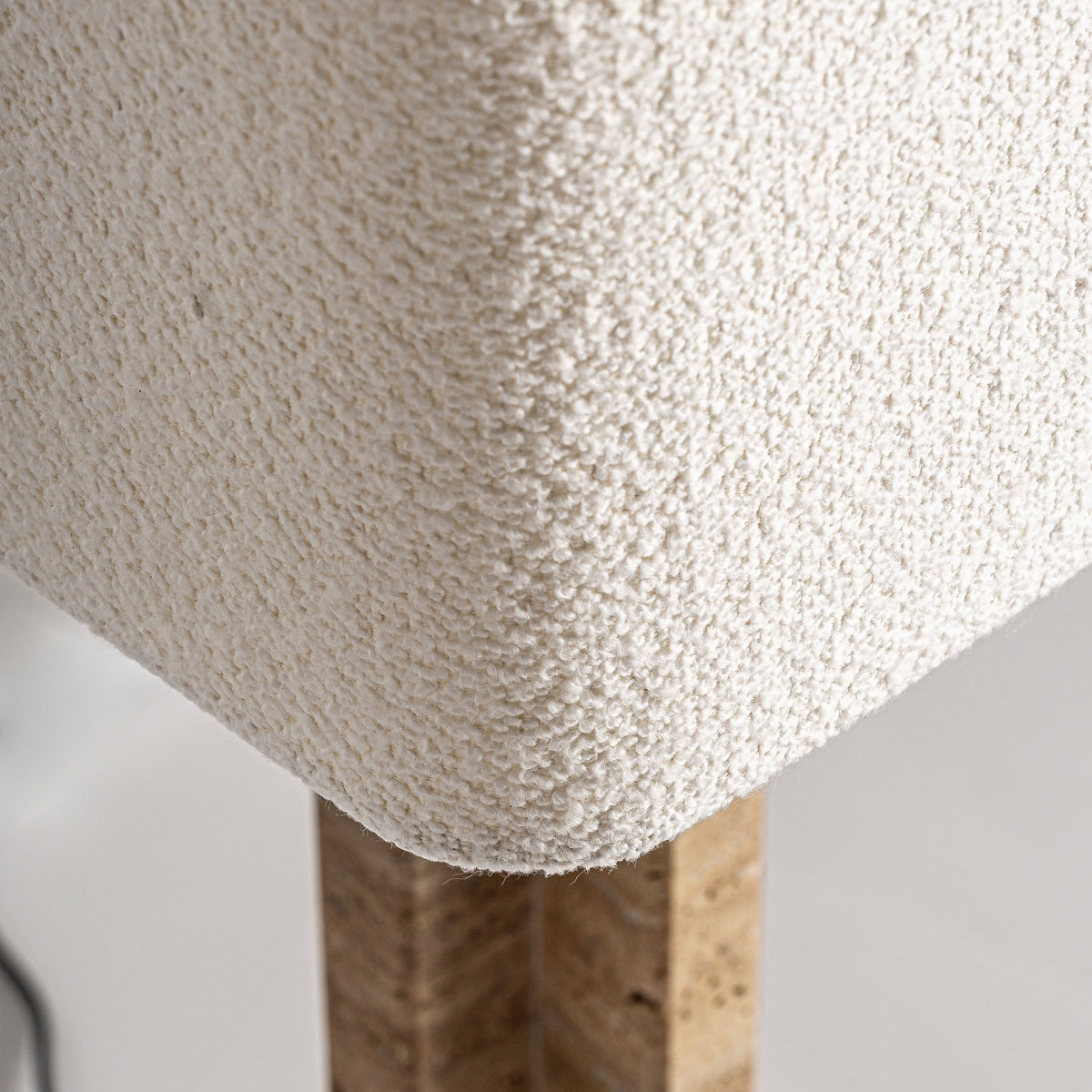 Primer plano de la esquina de un mueble tapizado en color blanco roto con textura y una lámpara de mesa en Travertino y hierro Trojan, perfecta para complementar la decoración de espacios vintage.