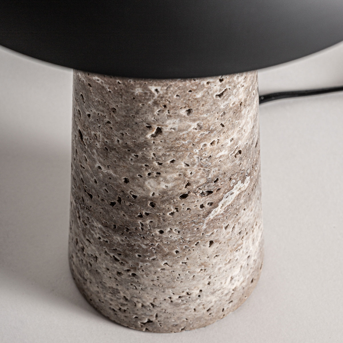 La Lámpara de mesa en mármol y hierro Dakia presenta una base cilíndrica con textura en tonos marrón y beige, rematada por una pantalla negra—una elegante referencia al diseño art déco.