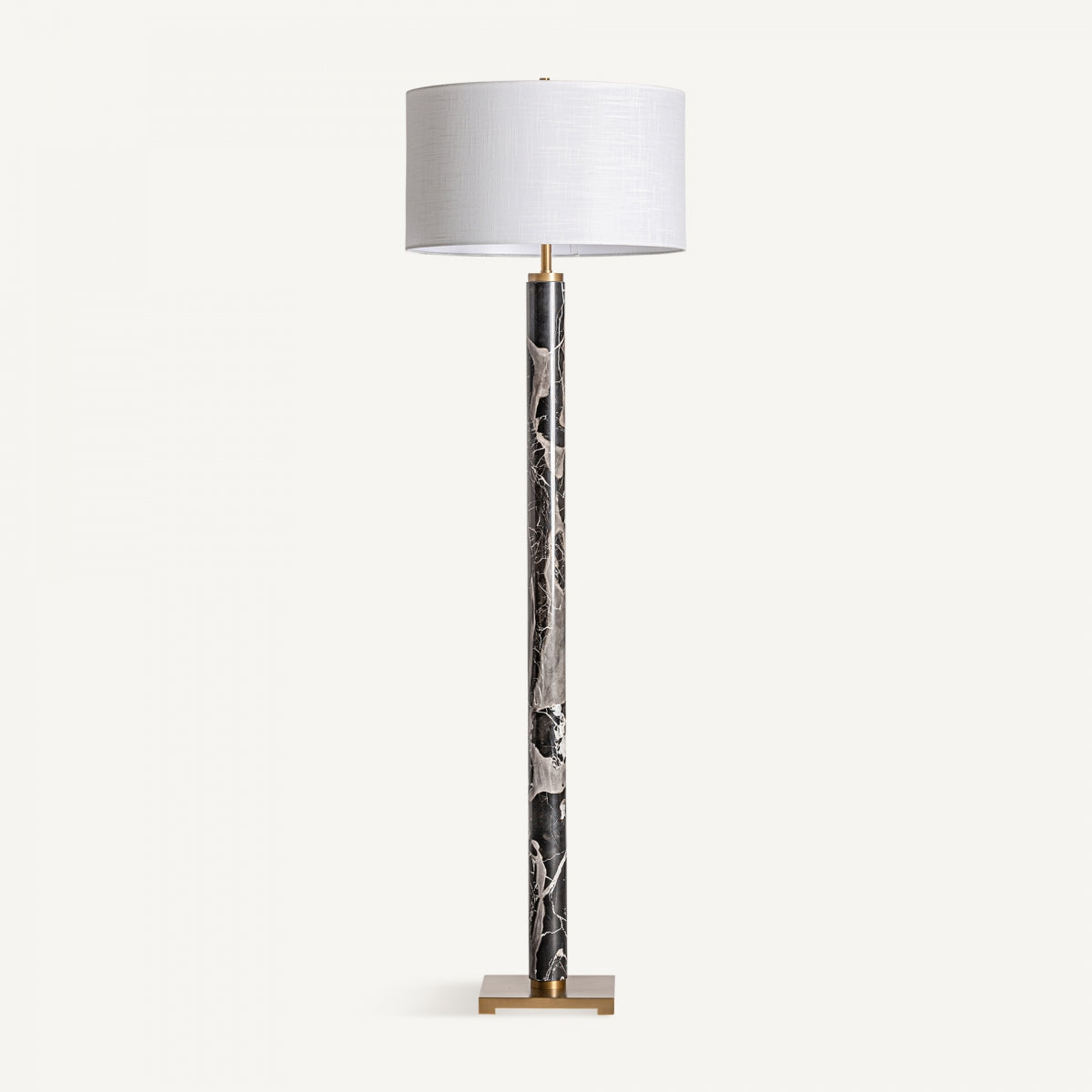 La Lámpara de pie en hierro y mármol Leora, con pantalla cilíndrica blanca, tallo con estampado de mármol negro y base cuadrada dorada, ofrece diseño exclusivo e iluminación sofisticada para cualquier espacio sobre fondo blanco.
