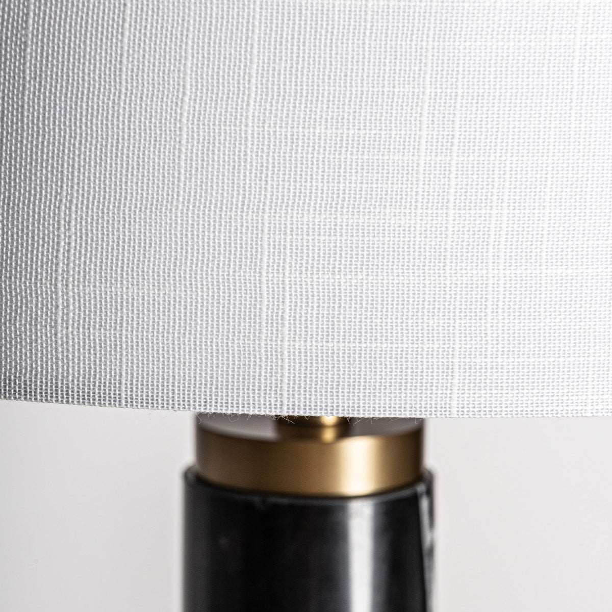 Primer plano de una pantalla texturizada en blanco con base cilíndrica de latón y negro de la Lámpara de pie en hierro y mármol Leora, ideal para quienes buscan iluminación sofisticada.