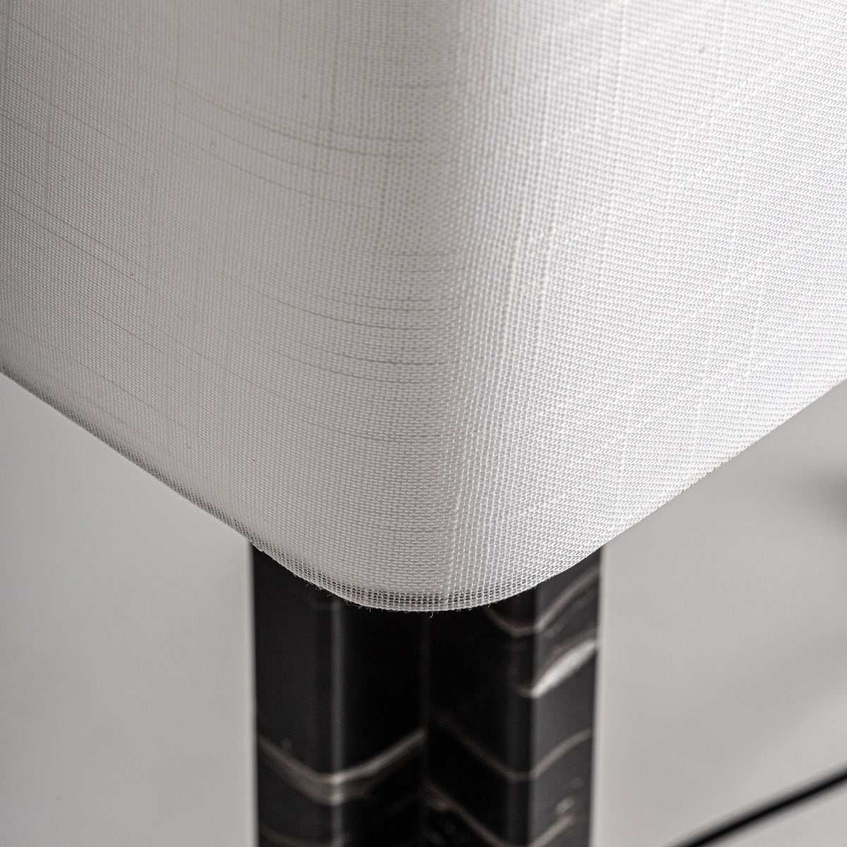 Primer plano de un mueble rincón tapizado en blanco con tela texturizada, sostenido por patas cilíndricas inspiradas en el acabado mármol negro de la Lámpara de mesa en mármol y hierro Artdec.