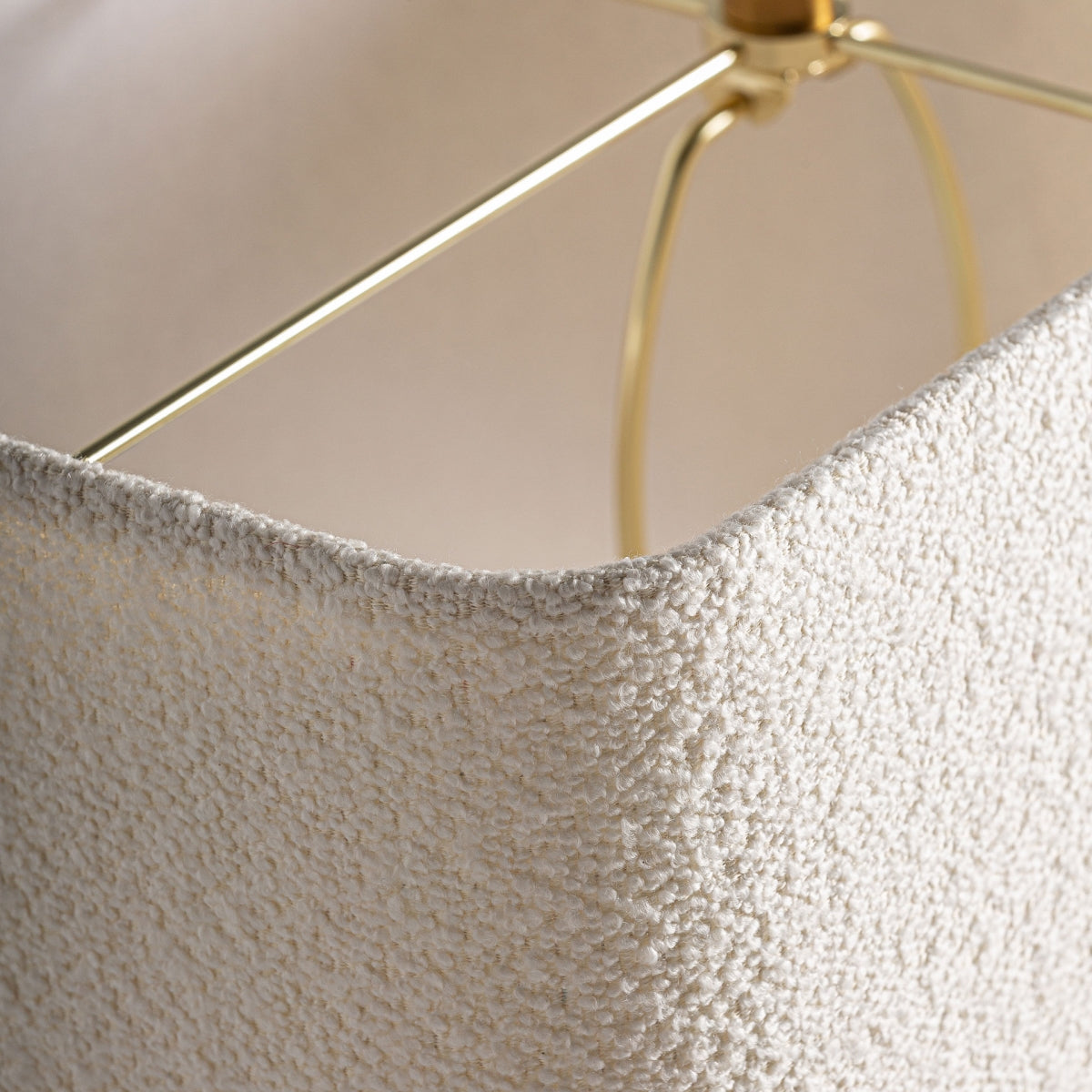 Primer plano de la pantalla texturizada de color crema de la Lámpara de mesa en travertino y hierro Fyfty, con soporte de metal dorado, proyectando una luz cálida sobre la habitación.