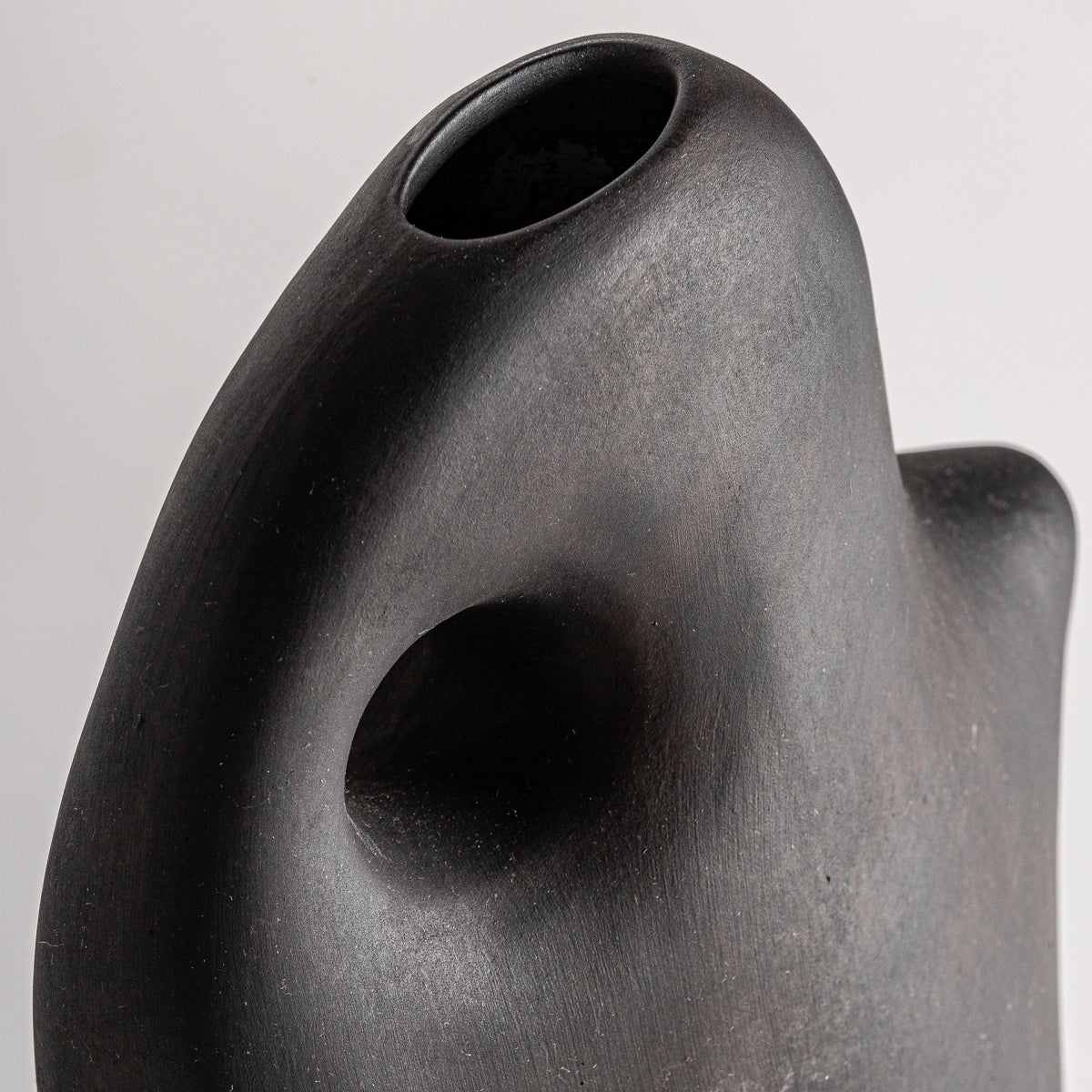 Primer plano del jarrón abstracto de cerámica negro Nohae N, que presenta una superficie lisa y una abertura ovalada con curvas fluidas contemporáneas y una hendidura redondeada.