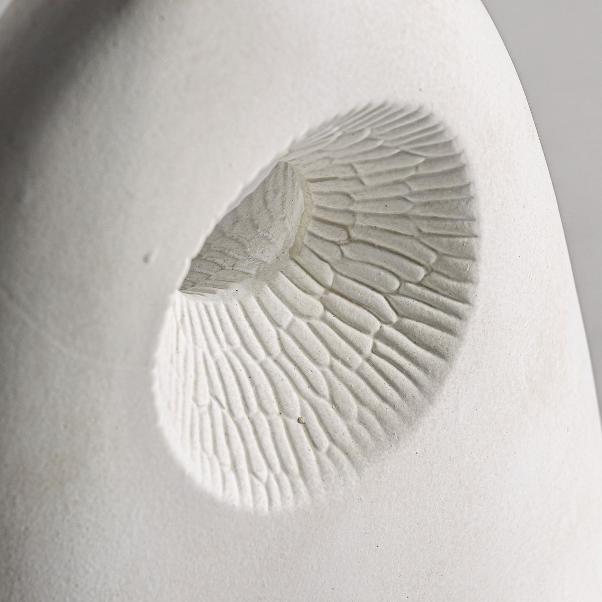 Un primer plano del Jarrón en cerámica art deco Leghe X revela su superficie texturizada en blanco con un patrón circular hundido que recuerda a escamas o pétalos, creando un diseño simétrico y minimalista realzado por detalles sombreados.