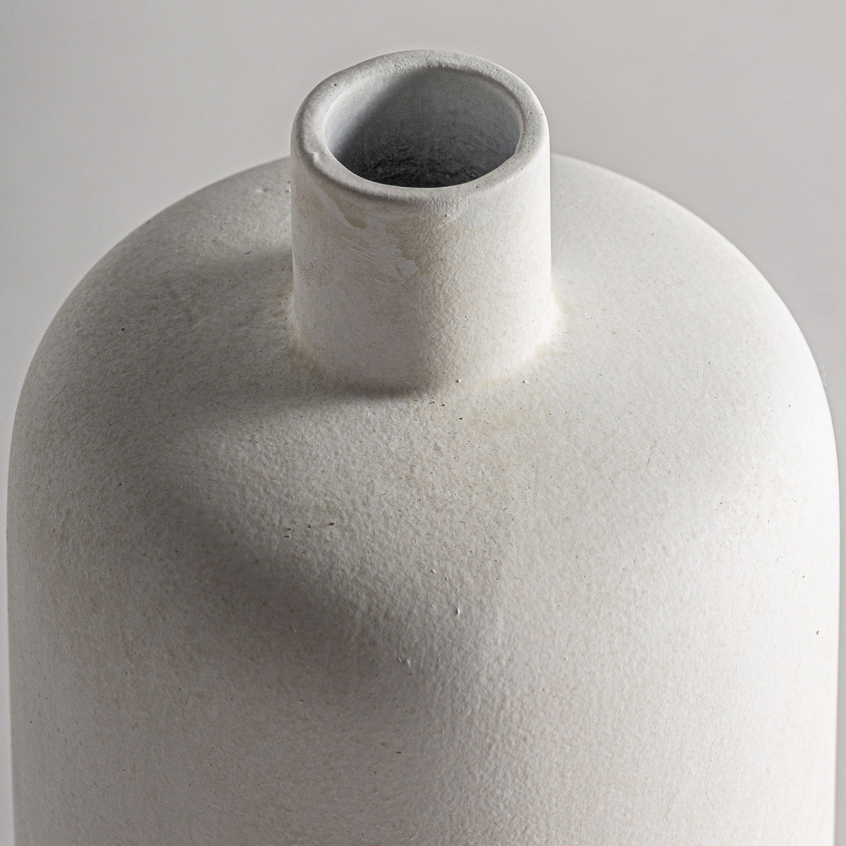 Primer plano del Jarrón de cerámica blanco LEGHE S, una elegante pieza art déco de cerámica blanca texturizada de alta calidad. Este jarrón minimalista presenta un cuello estrecho y un cuerpo liso y redondeado con una abertura ligeramente descentrada.