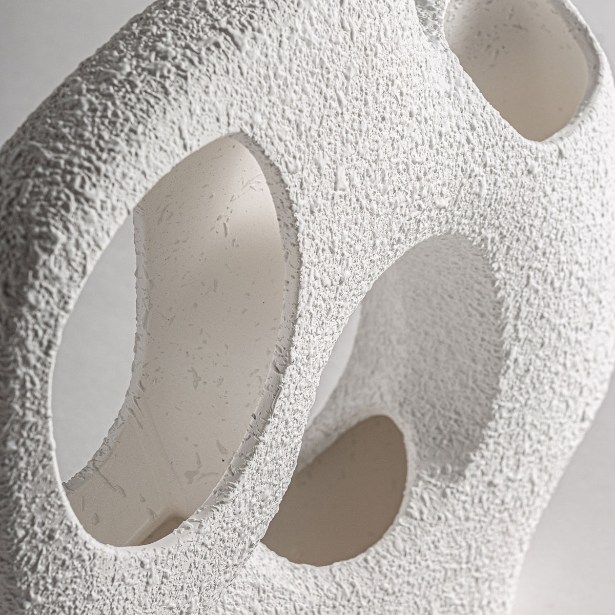 Primer plano de la Figura decorativa en cerámica blanca Gissel S, que presenta una escultura abstracta blanca texturizada con múltiples aberturas circulares, sobre un fondo liso, que encarna el diseño moderno.