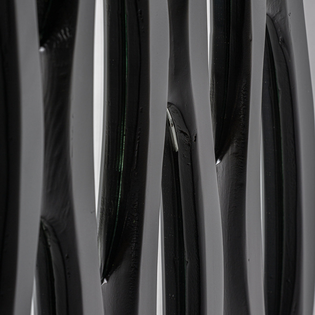 Primer plano de Espejo decorativo en madera negra (73x101 cm) Riley: varios elementos escultóricos verticales de color negro brillante con superficies lisas y curvas sutiles, que muestran exclusividad y encanto artesanal en una pieza decorativa contemporánea.