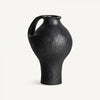 El Jarrón de resina negra Riley S es un jarrón de cerámica negra texturizada con una sola asa, cuerpo bulboso y cuello estrecho, perfecto para la decoración de interiores. Destaca elegantemente sobre un fondo blanco liso.