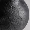 Primer plano del Jarrón de resina negra Riley S, que muestra su superficie oscura y texturizada, similar a una luna o una roca volcánica. Elaborado en resina negra con detalles irregulares y sutilmente iluminado en la parte superior derecha, es una pieza fascinante para la decoración de interiores.