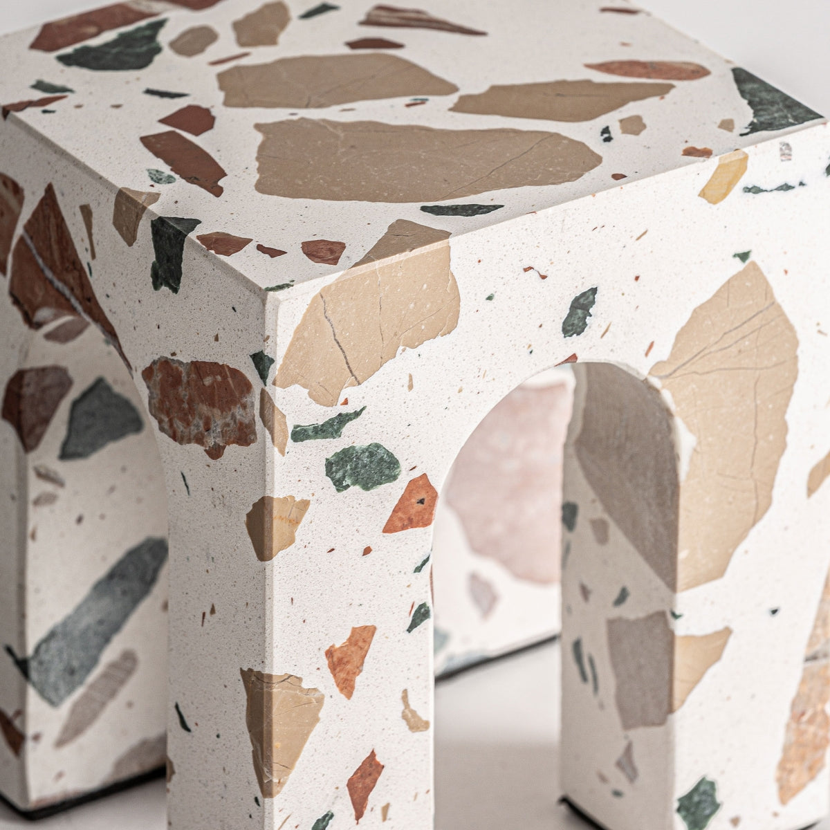 Un primer plano de la figura decorativa en mármol multicolor Asgard B, que muestra su base blanca con fragmentos de mármol multicolor incrustados y un distintivo diseño de patas en forma de arco.