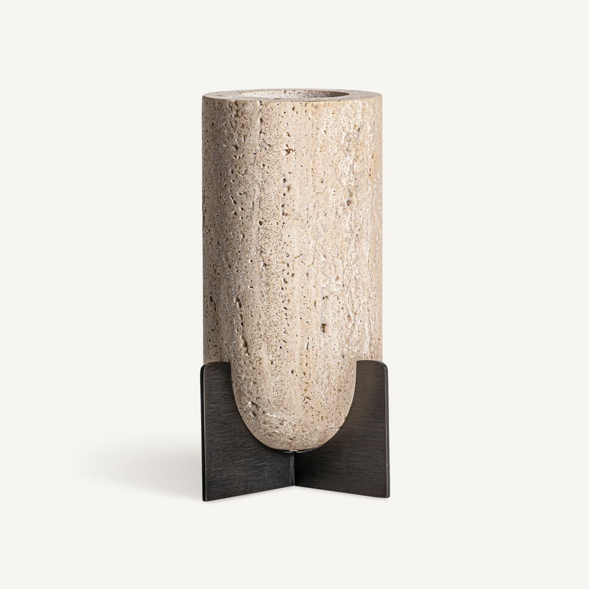 El Portavelas en travertino y hierro Asher, un jarrón cilíndrico inspirado en el beige travertino, está colocado sobre un soporte de metal oscuro en forma de cruz sobre un fondo blanco liso.