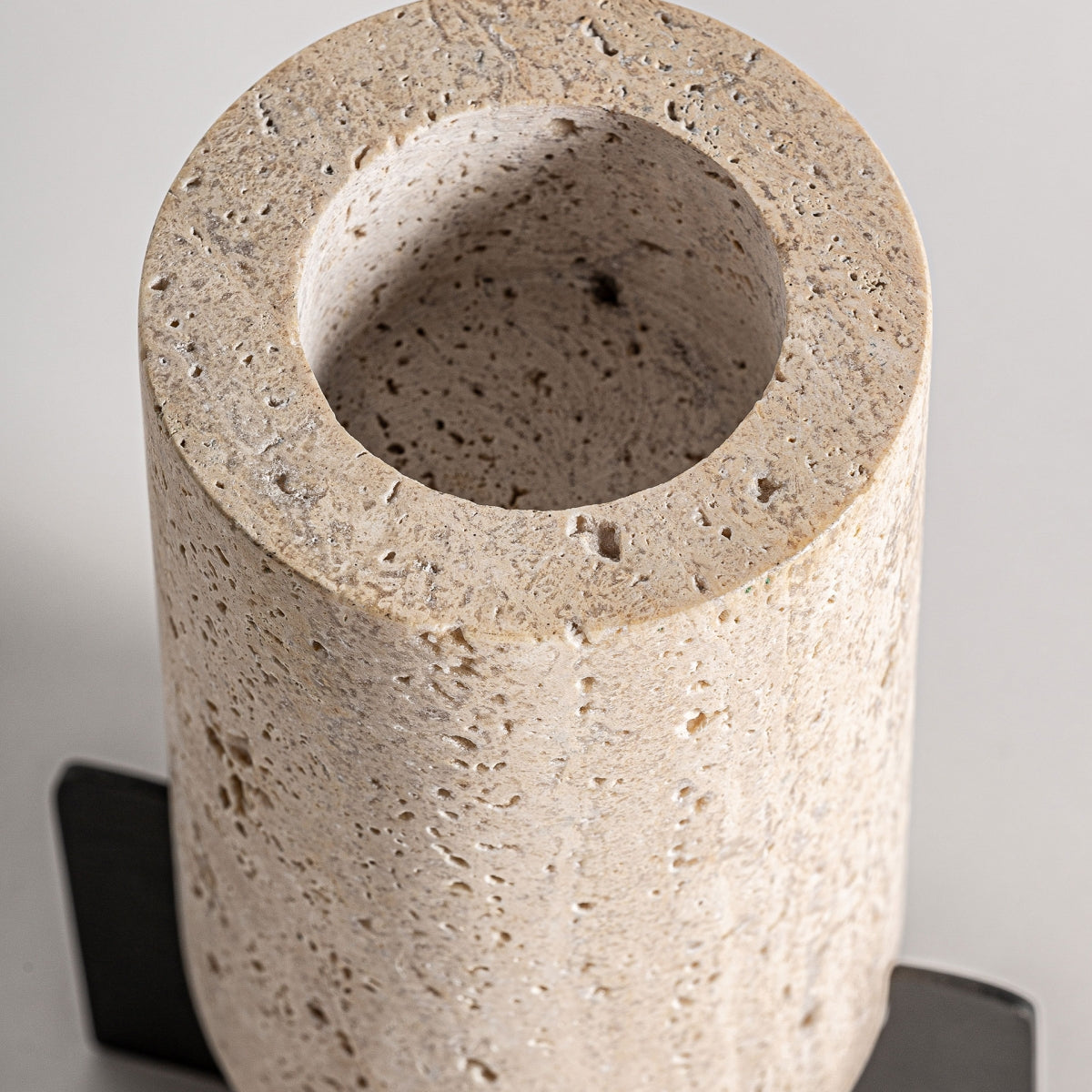 El portavelas de travertino y hierro Asher es un candelabro cilíndrico de textura rugosa y tapa hueca, que reposa sobre una base plana y oscura. Su elegante diseño art déco infunde un encanto atemporal a cualquier ambiente.