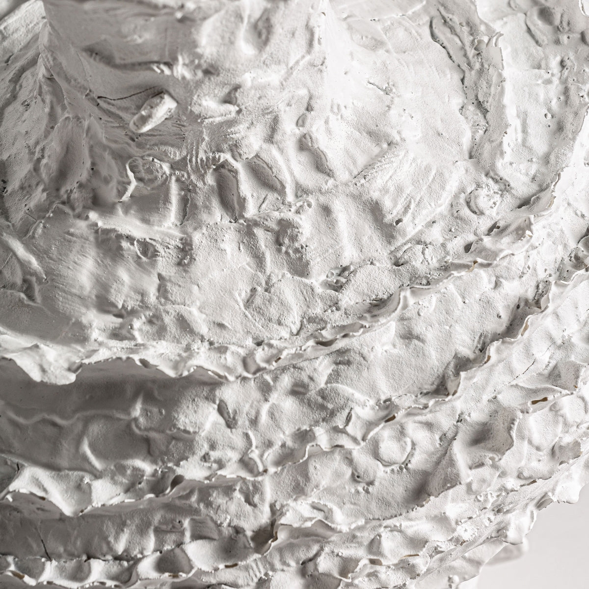 Primer plano de una superficie de yeso blanco texturizado con crestas y ranuras rugosas, ideal para decoración de interiores o para combinar con el Jarrón en resina blanco Basilio.