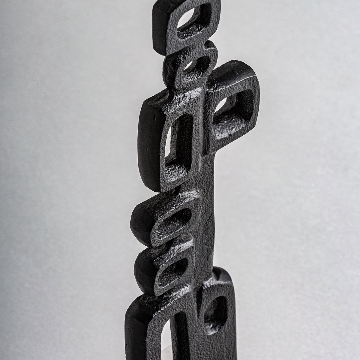 La figura decorativa de aluminio y mármol Dae encarna el diseño moderno, combinando a la perfección la estética y el estilo contemporáneo con su escultura abstracta de metal negro que presenta formas rectangulares y curvas apiladas verticalmente sobre un fondo gris.