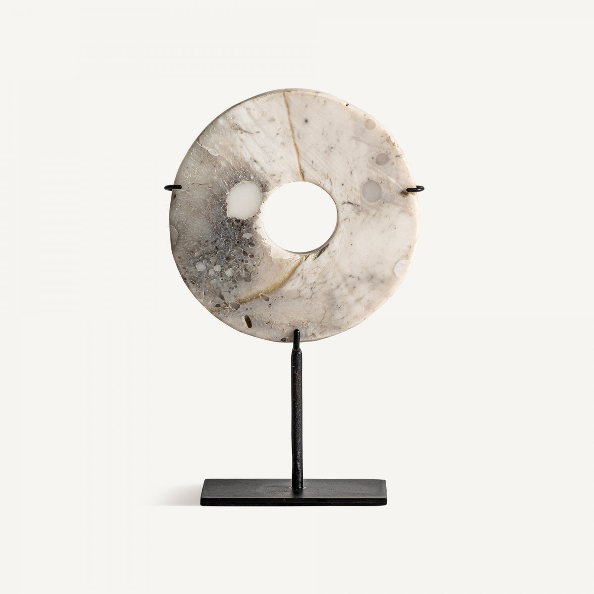 La Figura decorativa en hierro y piedra Agatha presenta un disco redondo de mármol con orificio central, montado verticalmente sobre una base rectangular negra, ideal para ambientes modernos.
