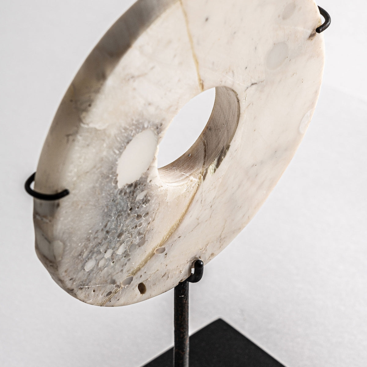 La Figura decorativa en hierro y piedra Agatha es una piedra blanca redonda y plana con un orificio central, montada verticalmente sobre una base negra, ideal para decoración moderna y espacios de diseño nórdico.