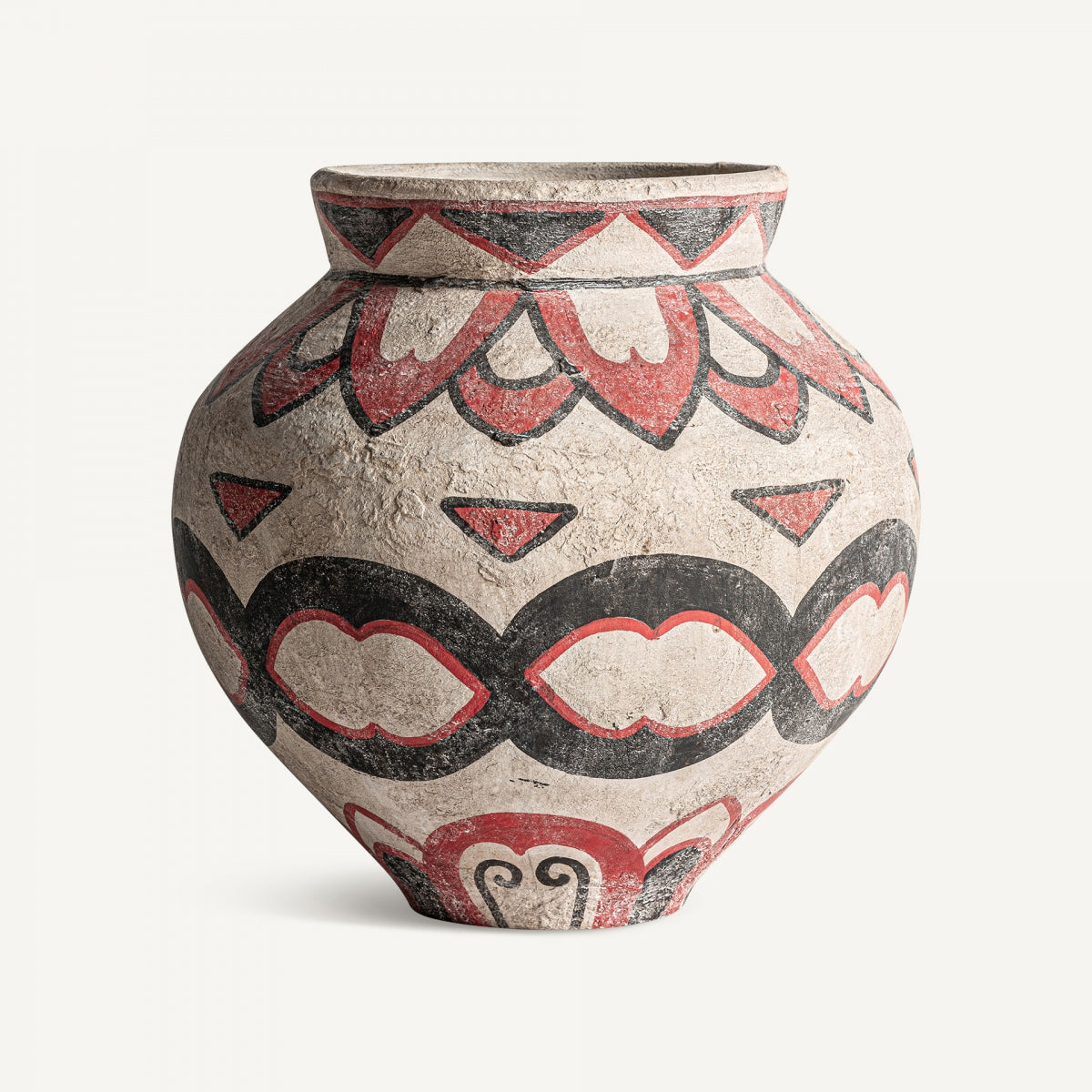 El jarrón en terracota multicolor Deosio es redondo y de cuerpo ancho, con patrones geométricos y curvilíneos en rojo y negro de inspiración étnica sobre una superficie de terracota clara.