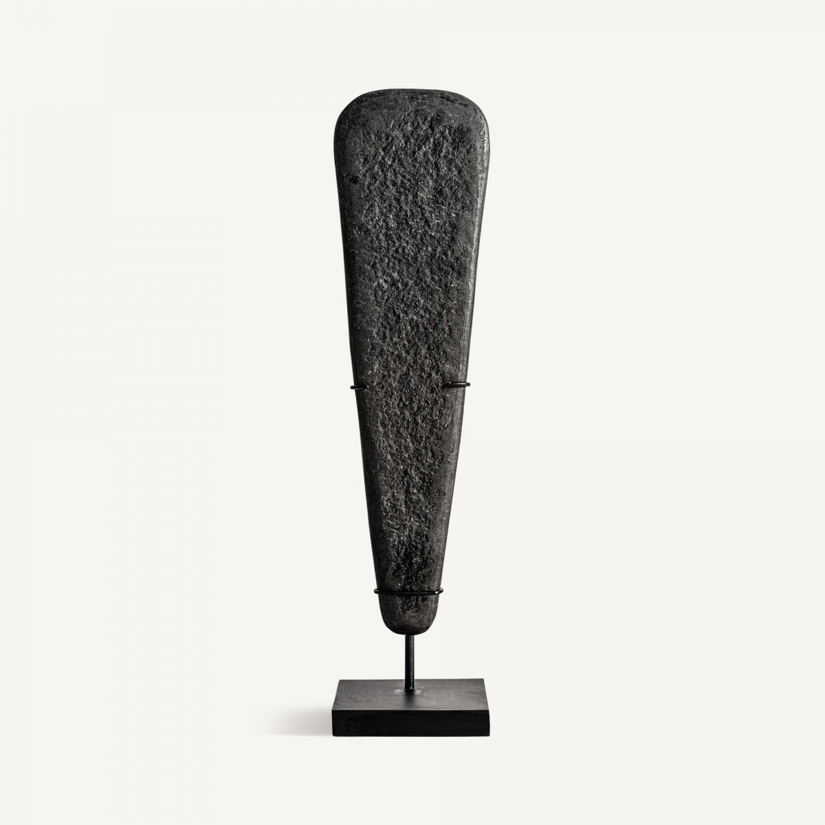 Una Figura decorativa en hierro y piedra Stone S, oscura y alargada, se alza verticalmente sobre un sencillo soporte negro sobre un fondo blanco liso, destacando el trabajo artesanal como escultura decorativa.