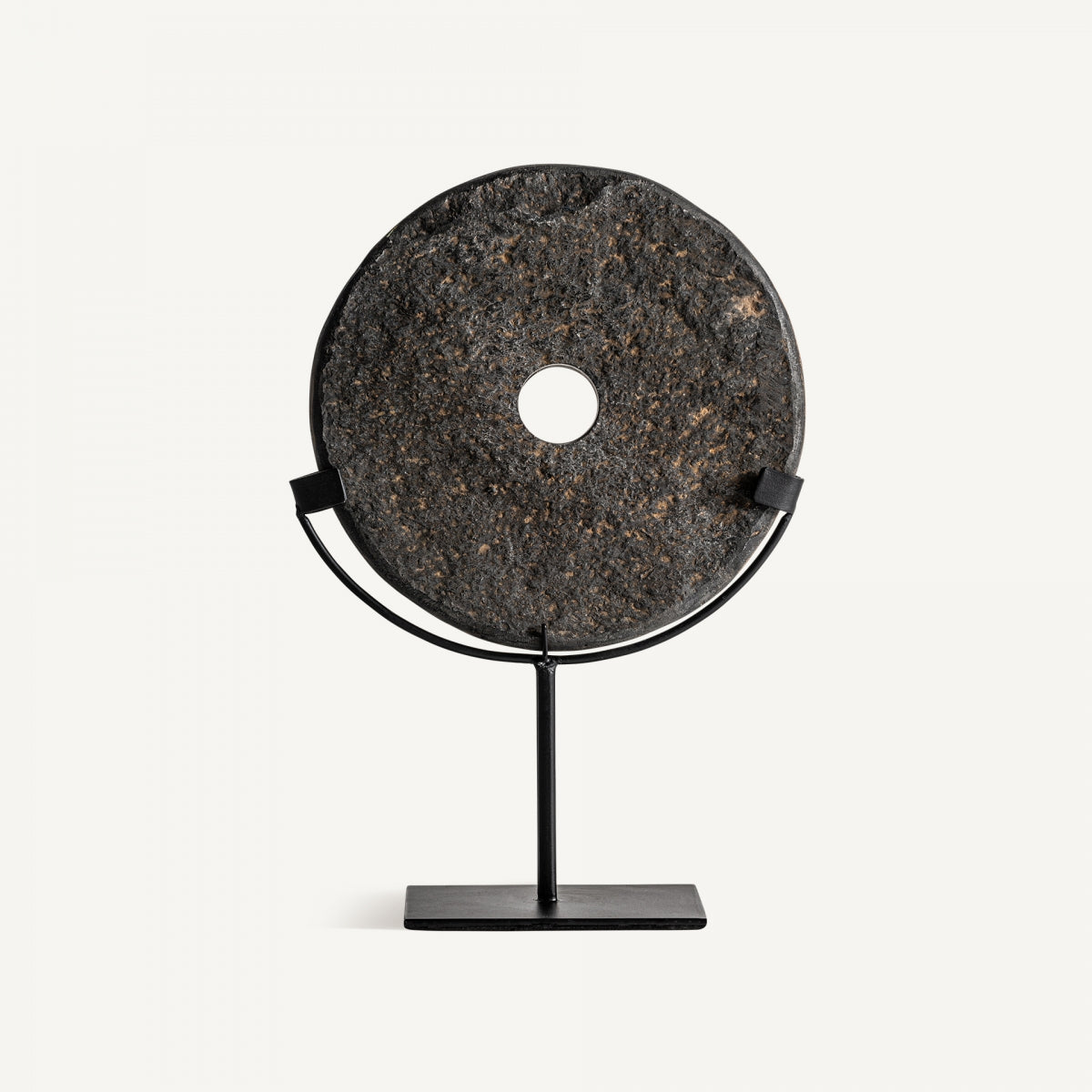 La Figura decorativa disco en piedra y hierro Seoane S, con forma circular y un orificio central, se exhibe en un soporte minimalista de hierro negro sobre fondo blanco, aportando estilo moderno y personalidad a cualquier espacio.