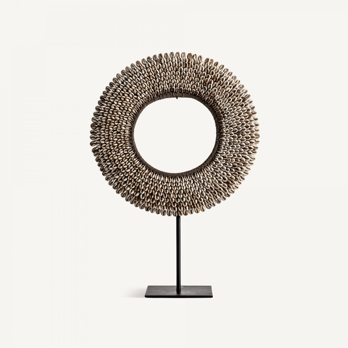La Figura decorativa Disco en hierro y conchas Janha, hecha de pequeñas conchas marrones en filas sobre un soporte de hierro negro, destaca su diseño étnico sobre fondo blanco.