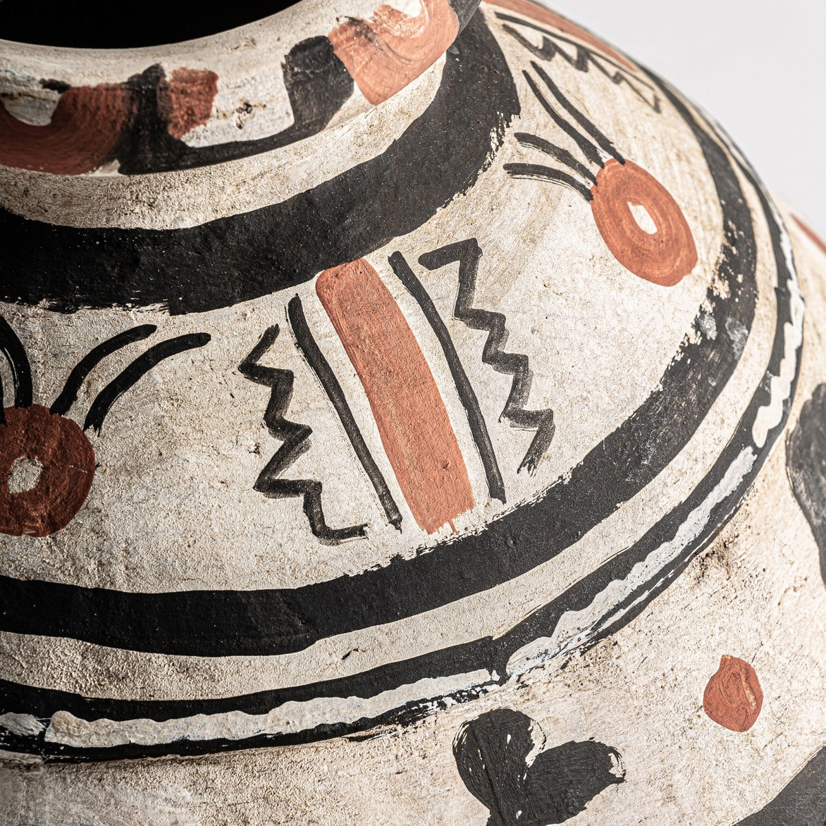 Primer plano del jarrón étnico en terracota Babil, que muestra diseños geométricos y abstractos en negro y marrón rojizo sobre una base de terracota ligera de alta calidad.