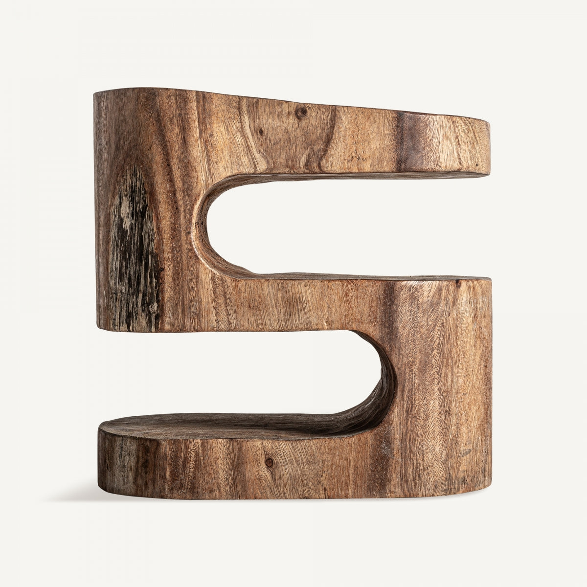La mesa auxiliar étnica en madera Kilkis presenta una escultura de madera en forma de S elaborada con madera de suar con un acabado suave y patrones de vetas visibles, que se mantiene en posición vertical sobre un fondo liso y emana vibraciones de diseño étnico.