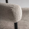 Primer plano de un apoyabrazos de tela beige texturizada en la Silla de comedor moderna tapizada y acero Albula, que presenta un elegante marco de metal y una estructura de poliéster gris, sobre un fondo borroso.