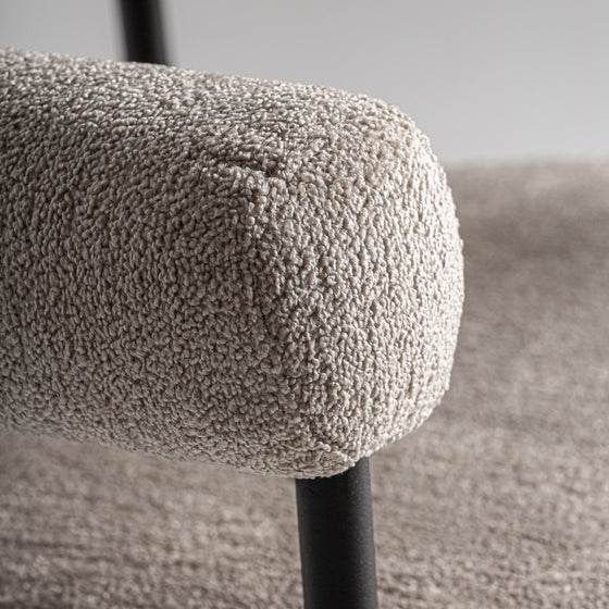 Primer plano de un apoyabrazos de tela beige texturizada en la Silla de comedor moderna tapizada y acero Albula, que presenta un elegante marco de metal y una estructura de poliéster gris, sobre un fondo borroso.