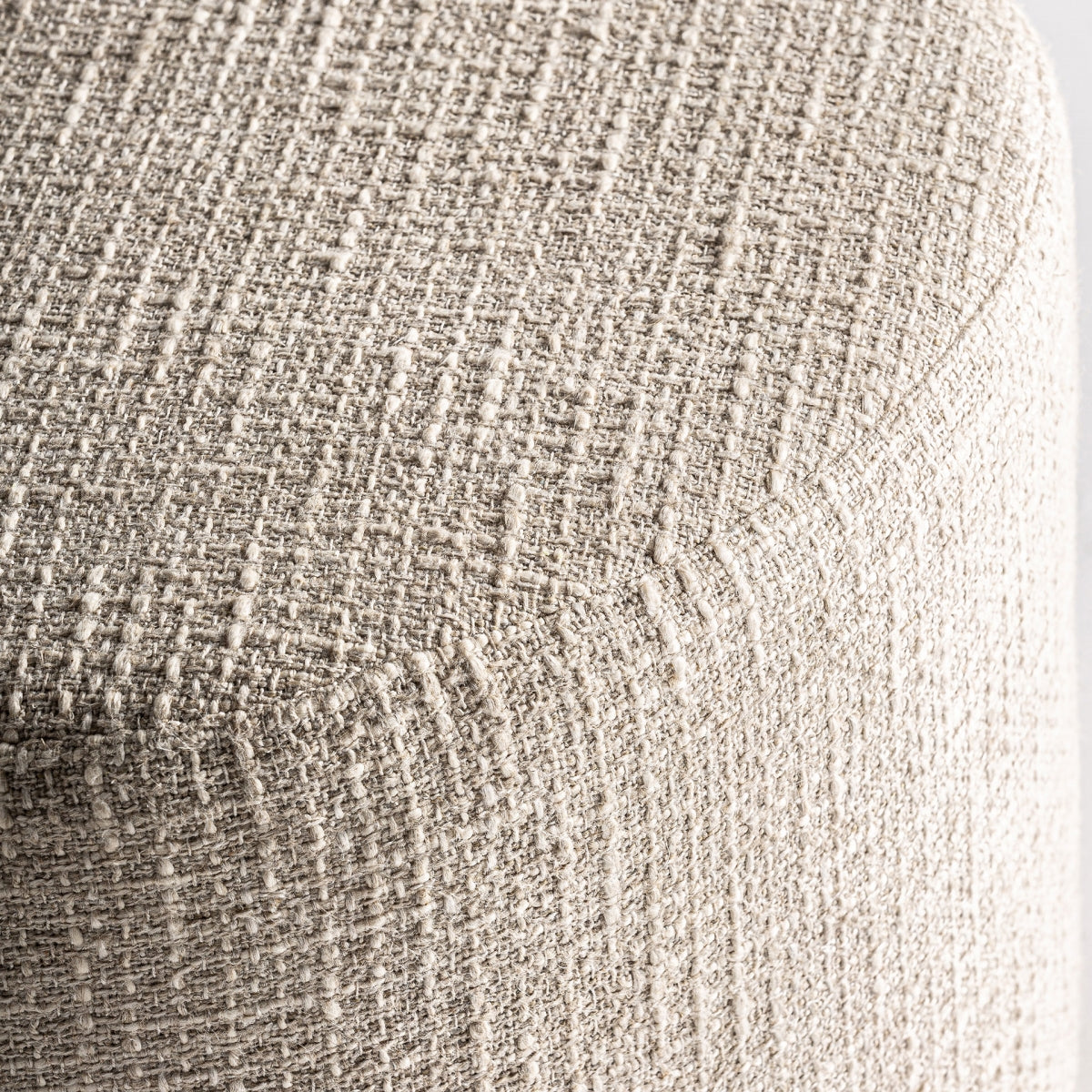 Primer plano de un tejido texturizado de color beige claro que cubre la esquina redondeada del Puff redondo en algodón y madera de mango Aran, resaltando su elegante diseño provenzal.