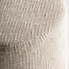Primer plano de un tejido texturizado de color beige claro que cubre la esquina redondeada del Puff redondo en algodón y madera de mango Aran, resaltando su elegante diseño provenzal.