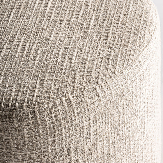 Primer plano de un tejido texturizado de color beige claro que cubre la esquina redondeada del Puff redondo en algodón y madera de mango Aran, resaltando su elegante diseño provenzal.