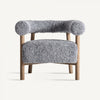 El sillón tapizado y madera de fresno Allitz es una silla moderna con patas de madera y tela gris texturizada redondeada en el asiento y el respaldo, que ejemplifica el diseño contemporáneo al tiempo que proporciona una comodidad excepcional sobre un fondo liso.