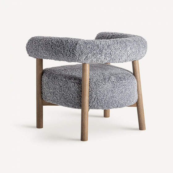 El sillón tapizado y madera de fresno Allitz combina comodidad y diseño contemporáneo con su tapizado gris lujoso, textura vellosa, respaldo redondeado y patas de madera sobre un fondo blanco liso.