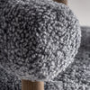 Un primer plano revela la tela gris texturizada, similar a la piel de oveja, del elegante Sillón tapizado y madera de fresno Allitz. Una pata de madera evoca un diseño contemporáneo y combina a la perfección estilo y comodidad en este mueble.