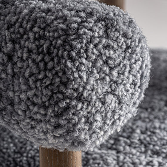 Un primer plano revela la tela gris texturizada, similar a la piel de oveja, del elegante Sillón tapizado y madera de fresno Allitz. Una pata de madera evoca un diseño contemporáneo y combina a la perfección estilo y comodidad en este mueble.