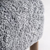Un primer plano muestra la suave tela de textura gris rizada colocada sobre un Sillón tapizado y madera de fresno Allitz de madera, resaltando su acabado artesanal y combinándose a la perfección con su diseño contemporáneo.