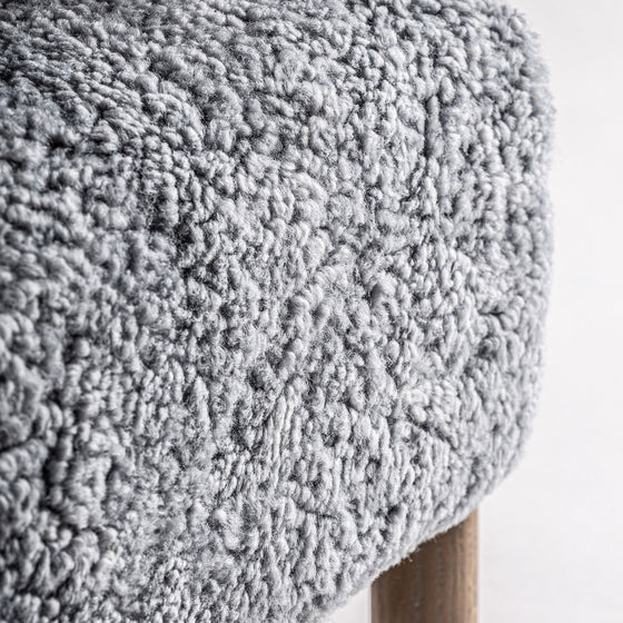 Un primer plano muestra la suave tela de textura gris rizada colocada sobre un Sillón tapizado y madera de fresno Allitz de madera, resaltando su acabado artesanal y combinándose a la perfección con su diseño contemporáneo.