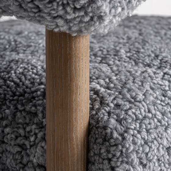 Primer plano de un poste de madera que sostiene una estructura de Sillón tapizado y madera de fresno Allitz recubierta de tela gris texturizada, que ofrece comodidad y se asemeja a la lana.