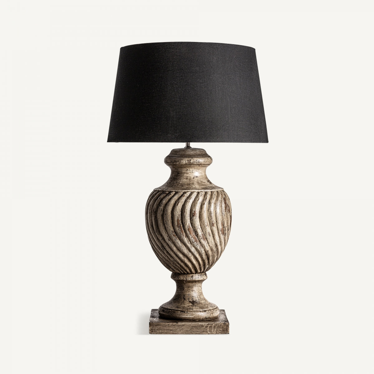 La lámpara de mesa en madera de mango Karua destaca por su base texturizada y tallada artesanalmente y su pantalla negra lisa, creando un contraste elegante sobre fondo blanco.