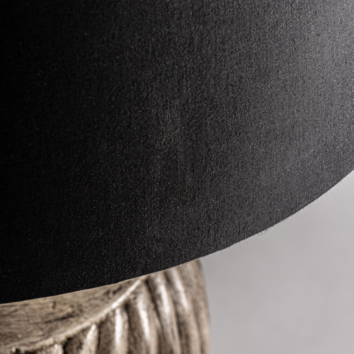 Primer plano de una pantalla negra texturizada con parte de una base de madera de mango claro a la vista, resaltando el diseño artesanal y elegante estilo colonial en la Lámpara de mesa en madera de mango Karua.