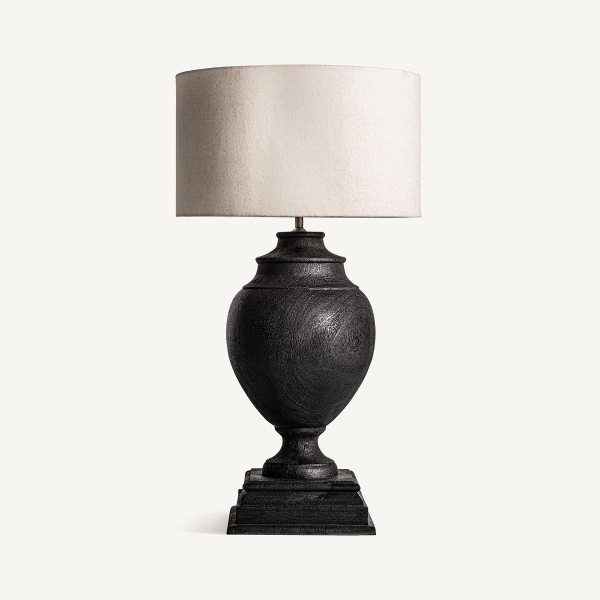 La Lámpara de sobremesa en madera de mango Ligia, con base negra en forma de urna y pantalla cilíndrica off-white, exuda elegancia artesanal sobre un fondo neutro.