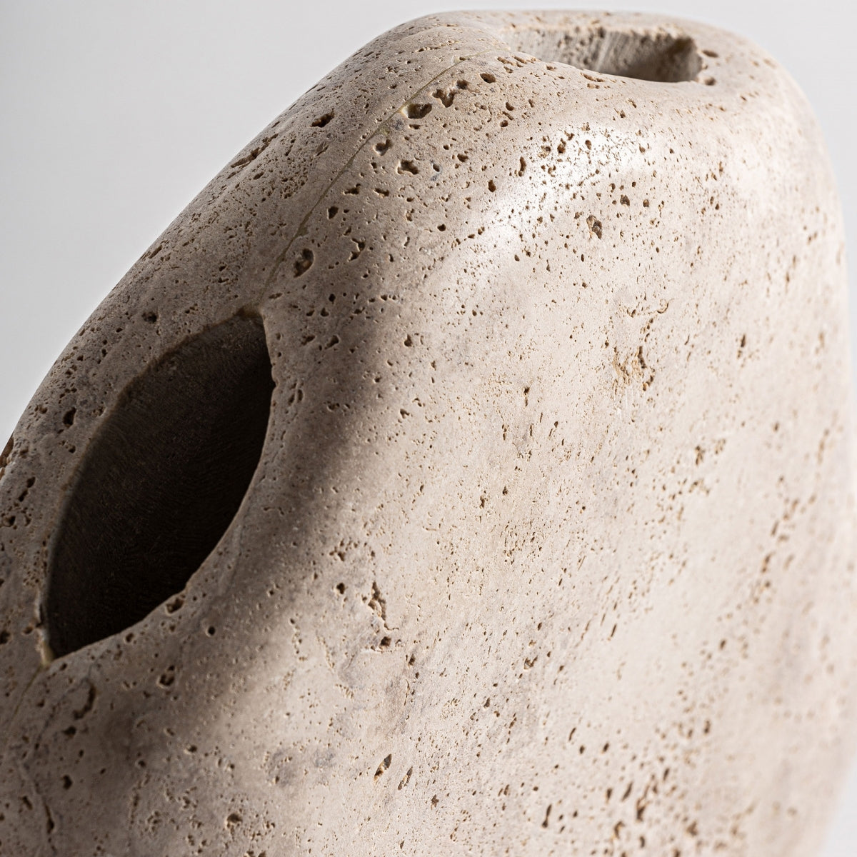 Primer plano del Jarrón contemporáneo en mármol Jasha, que presenta una piedra porosa de color beige con un borde redondeado y un orificio ovalado, que se asemeja al mármol crema y muestra un diseño moderno sobre fondo neutro.