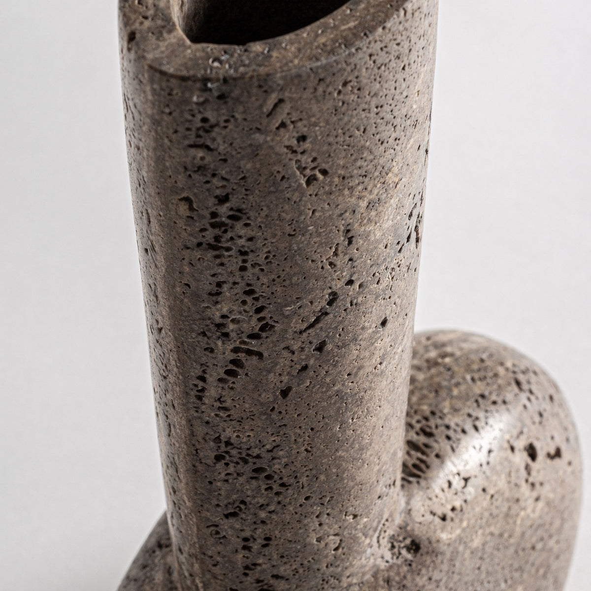 Detalle del Jarrón moderno en travertino Ander S, de sección vertical cilíndrica y base redondeada en travertino marrón, que muestra diseño contemporáneo sobre fondo liso.