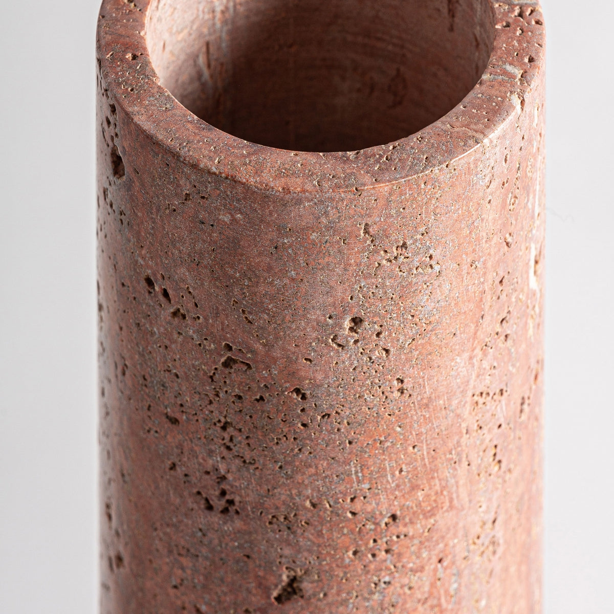 Primer plano del jarrón de mármol rosa Kleise S, un jarrón cilíndrico de textura rugosa y porosa y un borde liso y redondeado para un diseño elegante.