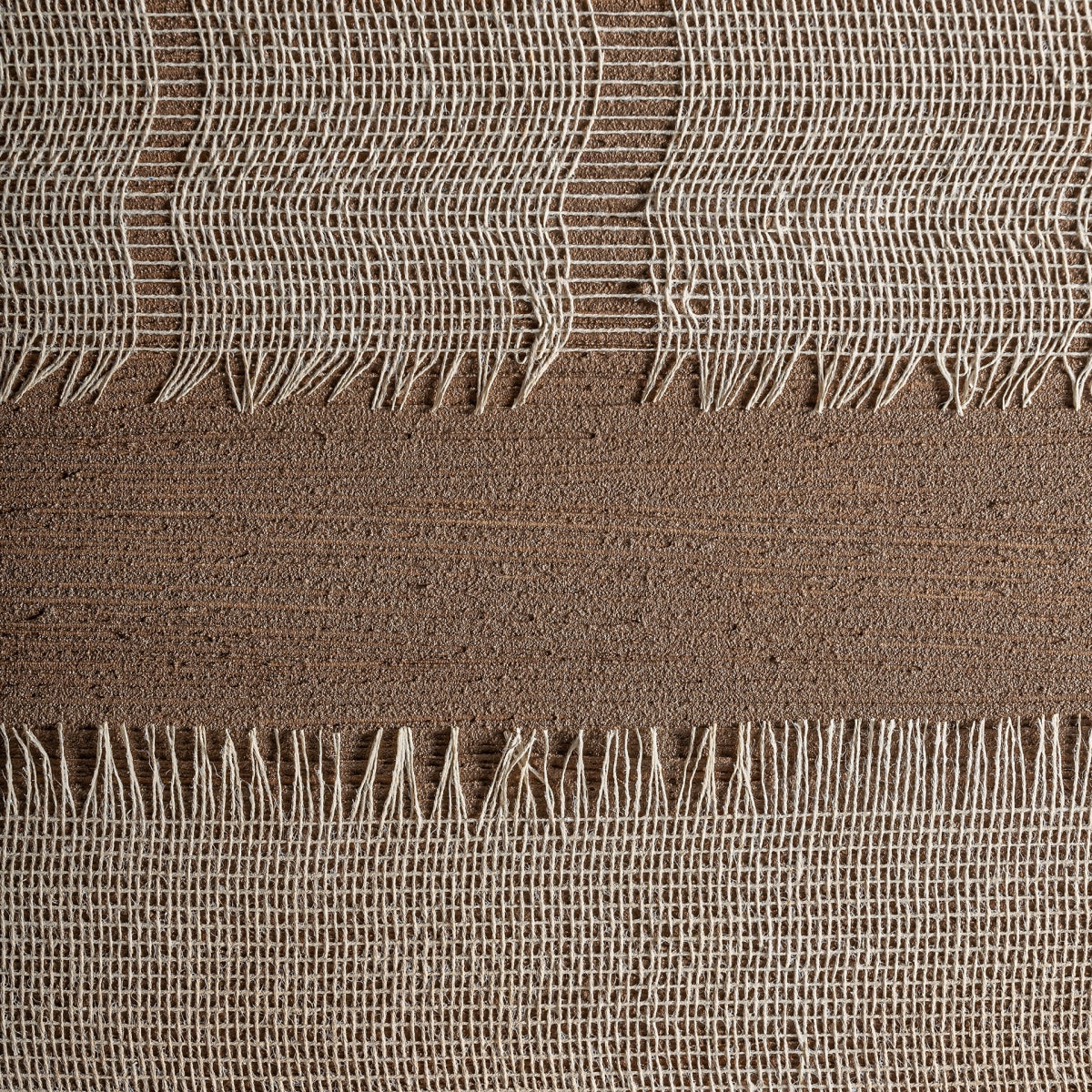 Primer plano de dos secciones de tela tejida beige con bordes deshilachados, separadas por una tira de material texturizado marrón, perfecto para una decoración moderna con el Cuadro lienzo colores marrones (150x220 cm) Dalmar de alta calidad.
