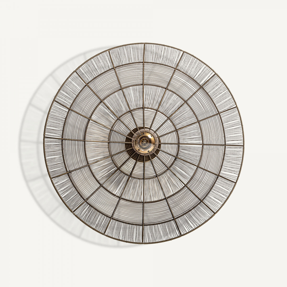 Aplique de pared en hierro bronce Bronna, de forma redonda con círculos concéntricos y líneas radiales, montado sobre fondo blanco y proyectando una sombra sutil para una iluminación elegante.