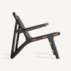 Una silla negra contemporánea con un diseño minimalista y líneas angulares, acentuada en naranja, aporta un toque de estilo vintage que recuerda al Sillón en madera de mango y piel Bourthes.